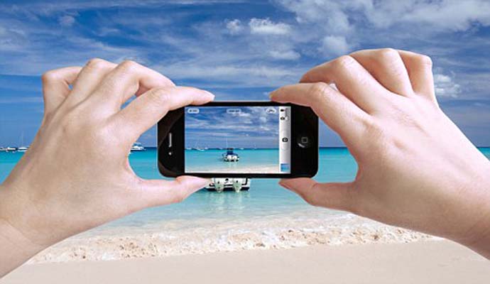 C1W97G Close up photo of a female tourist taking photos of a beautiful beach in The Bahamas with her iPhone 4 camera
