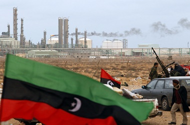 The Kingdom of Libya flag flies in front of a refinery in Ras Lanuf in this March 8, 2011, file photo. Libya's eastern city of Benghazi would risk fading back into obscurity after a six-month interlude as the seat of the rebel government were it not for one powerful asset: oil. Benghazi residents are struggling to convert their wartime sacrifices into economic clout to restore the status of a city once deemed on a par with the capital, Tripoli, and rescue it from its relative obscurity in the Muammar Gaddafi era. REUTERS/Goran Tomasevic/ Files (LIBYA - Tags: ENERGY BUSINESS CONFLICT POLITICS)
